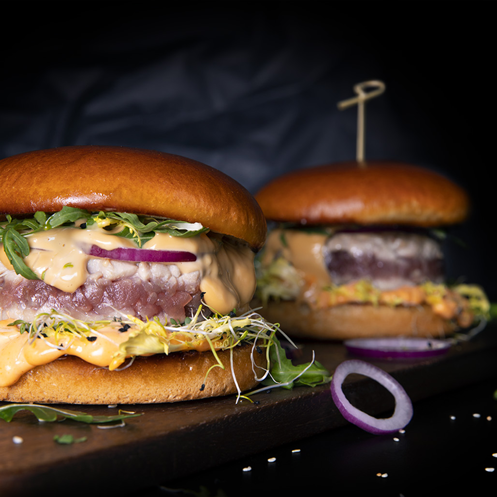 Frisch zubereiteter Shiso Tuna Burger Deluxe mit saftigem Thunfisch-Patty, knackigem Salat, asiatischen Toppings und würziger Sauce in einem goldbraunen Burger Bun serviert.